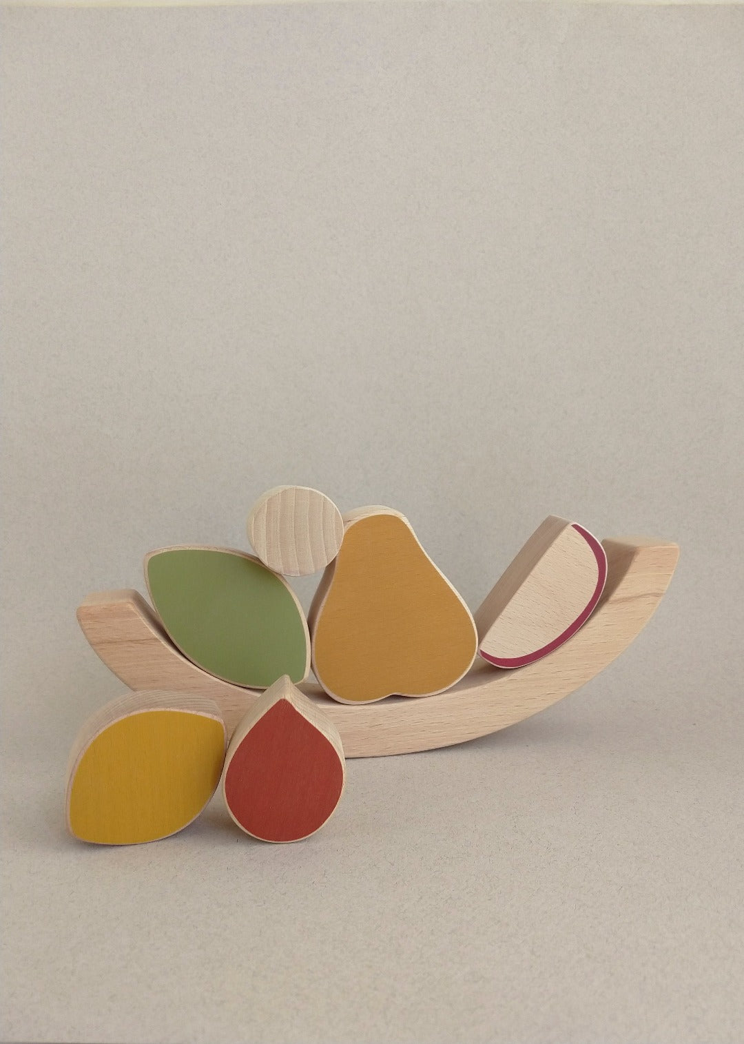 Abstract forms, satin smooth wood surfaces and warm colours invite the child to play while practicing fine motor skills by stacking the wooden fruits, leaves and seeds in the swinging concave form of the basket.